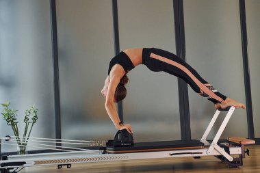Spor elbiseli ve zayıf vücutlu genç bir kadın kapalı alanda spor yoga yapıyor..
