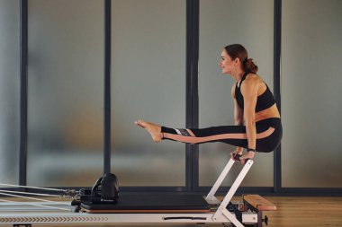 Spor elbiseli ve zayıf vücutlu genç bir kadın kapalı alanda spor yoga yapıyor..