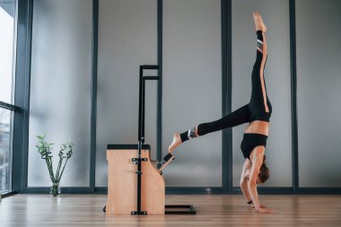 Spor elbiseli ve zayıf vücutlu genç bir kadın kapalı alanda spor yoga yapıyor..
