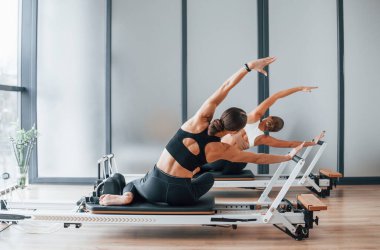 Spor aletlerini kullanarak. Spor elbiseli ve zayıf vücutlu iki kadın kapalı alanda spor yoga yapıyorlar..