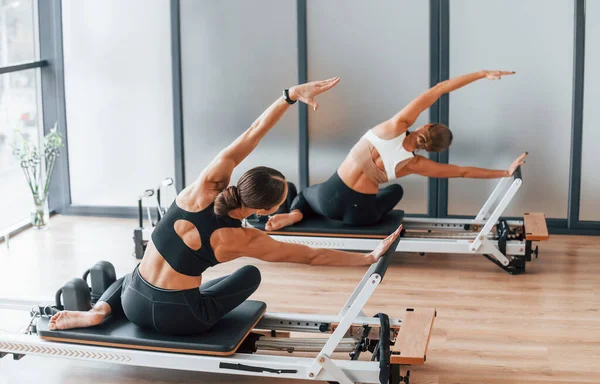 Spor aletlerini kullanarak. Spor elbiseli ve zayıf vücutlu iki kadın kapalı alanda spor yoga yapıyorlar..