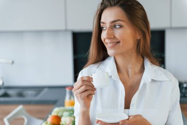 İçkili ve kurabiyeli fincan. Genç Avrupalı kadın içeride, mutfakta sağlıklı yiyeceklerle birlikte..