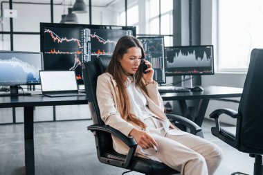 Telefonla konuşuyor. Genç bayan borsacı ofiste çalışıyor. Ekranların çoğu.