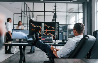 Adam sandalyeye oturur ve mola verir. Borsacılardan oluşan bir ekip modern ofiste birçok ekran ekranı ile çalışır..