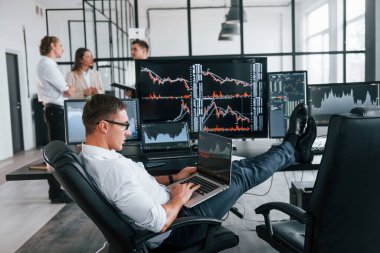 Gözlüklü adam işine odaklanmış. Borsacılardan oluşan ekip birçok ekranla modern ofiste..