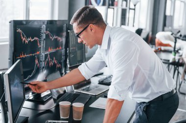 Resmi kıyafetlerle. Genç borsacı erkek ofis içinde çalışıyor. Ekranların çoğu.