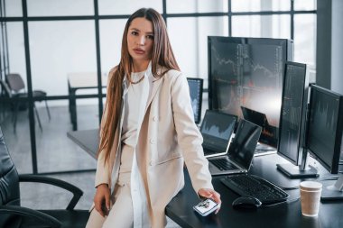 Kameraya poz ver. Genç bayan borsacı ofisin içinde. Ekranların çoğu.