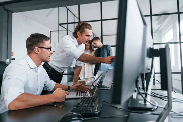 Guy in glasses concentrated at work. Team of stockbrokers is in modern office with many display screens.