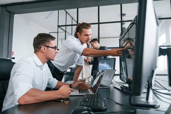 Guy in glasses concentrated at work. Team of stockbrokers is in modern office with many display screens.