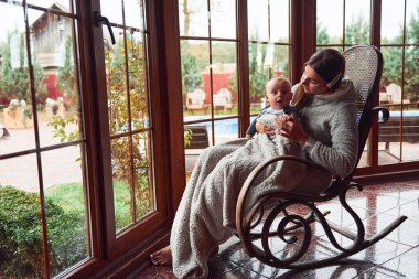 Mutlu anne oğlunun yanında pencerenin yanındaki sandalyede oturur..