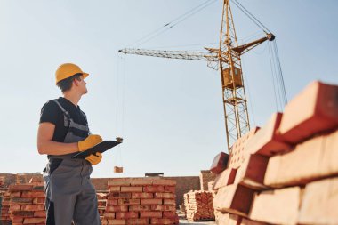 İçinde belgeler olan bir not defteri tutuyor. Üniformalı inşaat işçisi ve güvenlik ekipmanı inşaatında çalışıyor.