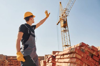 Vinçli adamla iletişim kuruyorum. Üniformalı inşaat işçisi ve güvenlik ekipmanı inşaatında çalışıyor.