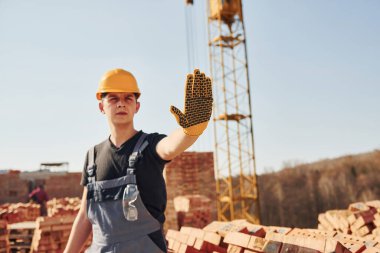 Dur işaretini elle gösterir. Üniformalı inşaat işçisi ve güvenlik ekipmanı inşaatında çalışıyor.