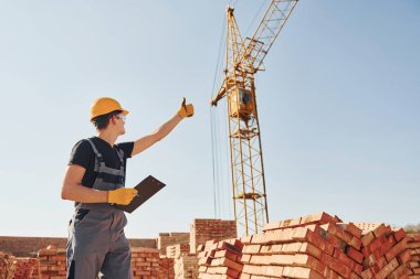Vinçli adamla iletişim kuruyorum. Üniformalı inşaat işçisi ve güvenlik ekipmanı inşaatında çalışıyor.