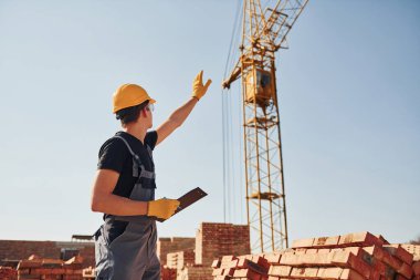 Vinçli adamla iletişim kuruyorum. Üniformalı inşaat işçisi ve güvenlik ekipmanı inşaatında çalışıyor.
