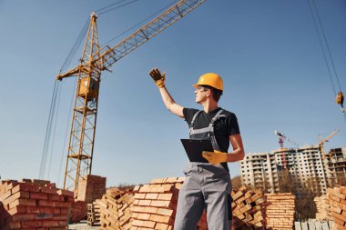 Communicating with crane guy. Construction worker in uniform and safety equipment have job on building.