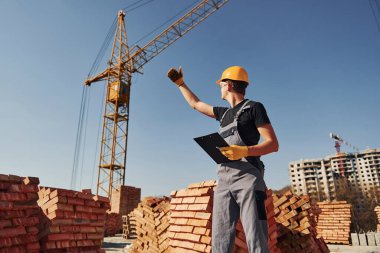 Vinçli adamla iletişim kuruyorum. Üniformalı inşaat işçisi ve güvenlik ekipmanı inşaatında çalışıyor.