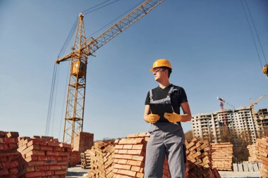 Holds notepad with documents. Construction worker in uniform and safety equipment have job on building.