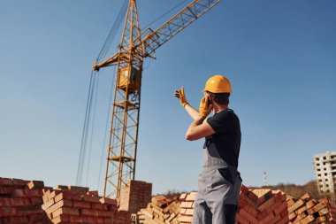 Communicating with crane guy. Construction worker in uniform and safety equipment have job on building.