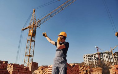 Talking by phone. Construction worker in uniform and safety equipment have job on building.