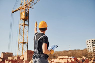 Vinçli adamla iletişim kuruyorum. Üniformalı inşaat işçisi ve güvenlik ekipmanı inşaatında çalışıyor.