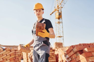 Tuğlayı elinde tutuyor. Üniformalı inşaat işçisi ve güvenlik ekipmanı inşaatında çalışıyor.