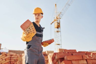 Holds brick in hand. Construction worker in uniform and safety equipment have job on building.