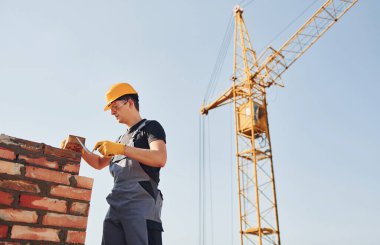 Tuğla duvar kuruluyor. Üniformalı inşaat işçisi ve güvenlik ekipmanı inşaatında çalışıyor.