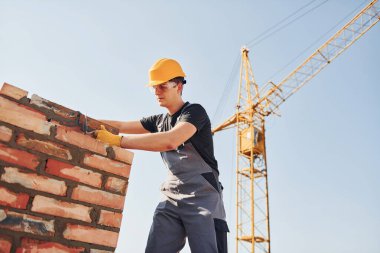 Tuğla duvar kuruluyor. Üniformalı inşaat işçisi ve güvenlik ekipmanı inşaatında çalışıyor.