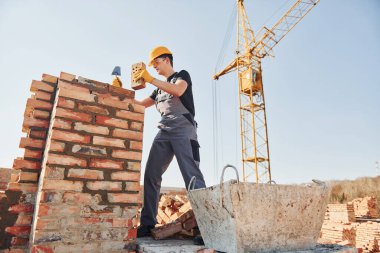 Tuğla duvar kuruluyor. Üniformalı inşaat işçisi ve güvenlik ekipmanı inşaatında çalışıyor.