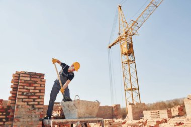 Galeri açıyorum. Üniformalı inşaat işçisi ve güvenlik ekipmanı inşaatında çalışıyor.