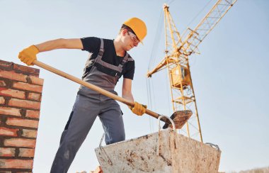 Using showel. Construction worker in uniform and safety equipment have job on building.