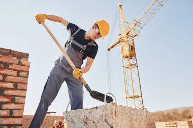 Galeri açıyorum. Üniformalı inşaat işçisi ve güvenlik ekipmanı inşaatında çalışıyor.