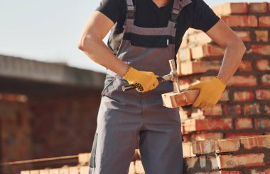 Tuğla duvarla meşgul. Üniformalı inşaat işçisi ve güvenlik ekipmanı inşaatında çalışıyor.