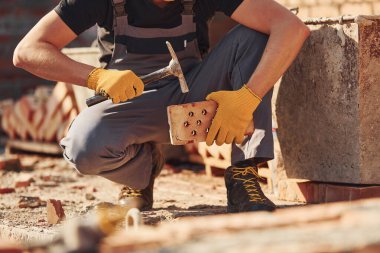 Construction worker in uniform and safety equipment sits and have job on building.