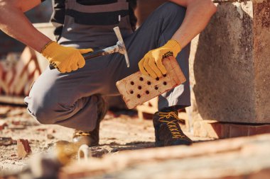 Construction worker in uniform and safety equipment sits and have job on building.