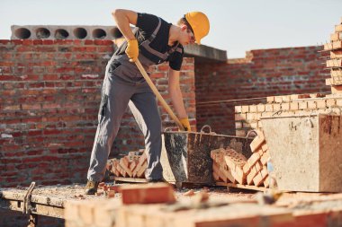 Using showel. Construction worker in uniform and safety equipment have job on building.