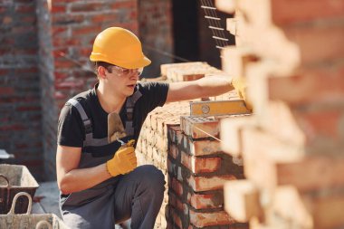 Measures of brick wall. Construction worker in uniform and safety equipment have job on building.
