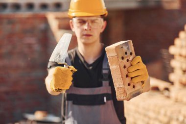 Üniformalı ve güvenlik ekipmanlı inşaat işçilerinin portresi tuğla ve aletlerle ayakta duruyor..