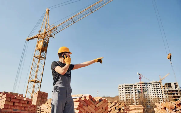 Telefonla konuşuyorum. Üniformalı inşaat işçisi ve güvenlik ekipmanı inşaatında çalışıyor.