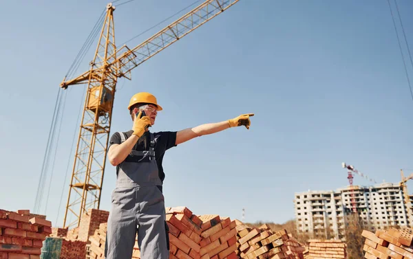 Talking by phone. Construction worker in uniform and safety equipment have job on building.