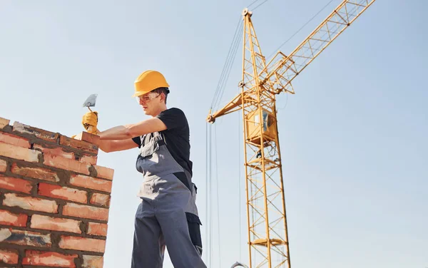 Tuğla duvar kuruluyor. Üniformalı inşaat işçisi ve güvenlik ekipmanı inşaatında çalışıyor.