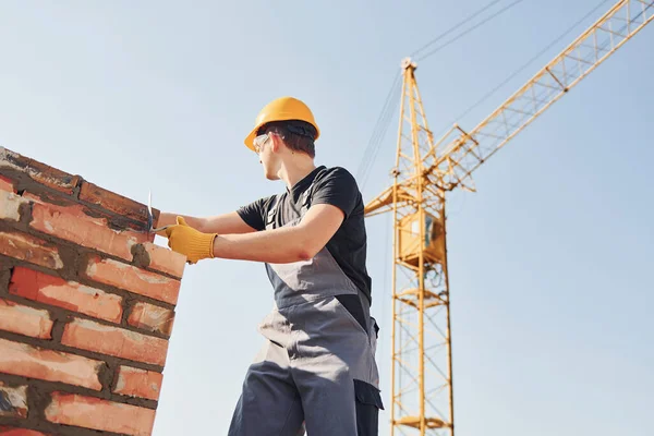 Tuğla duvar kuruluyor. Üniformalı inşaat işçisi ve güvenlik ekipmanı inşaatında çalışıyor.