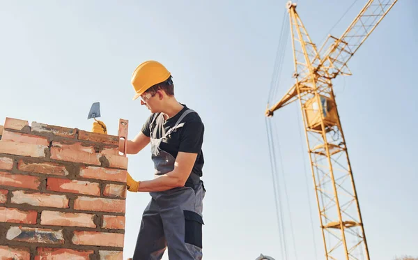 Tuğla duvar kuruluyor. Üniformalı inşaat işçisi ve güvenlik ekipmanı inşaatında çalışıyor.