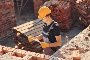 Planı kontrol altında tutuyoruz. Üniformalı inşaat işçisi ve güvenlik ekipmanı inşaatında çalışıyor.