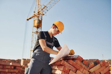 Planı kontrol altında tutuyoruz. Üniformalı inşaat işçisi ve güvenlik ekipmanı inşaatında çalışıyor.