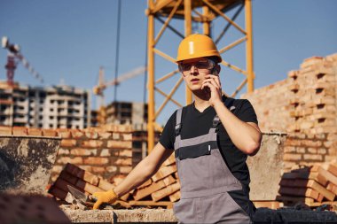Talking by phone. Construction worker in uniform and safety equipment have job on building.