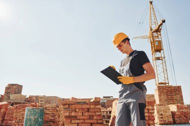 İçinde belgeler olan bir not defteri tutuyor. Üniformalı inşaat işçisi ve güvenlik ekipmanı inşaatında çalışıyor.