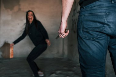 Rear view of psycho with knife that follow young girl in abandoned building.