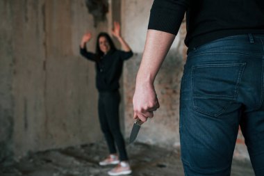 Rear view of psycho with knife that follow young girl in abandoned building.